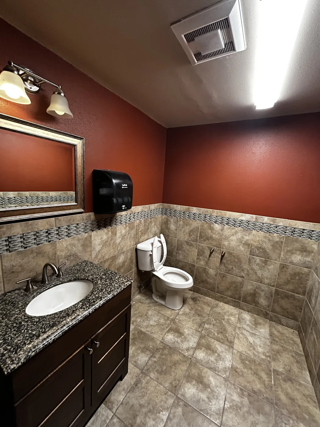 Completed commercial restroom in Lakewood, WA — tile wainscot with mosaic accent band and granite-top vanity