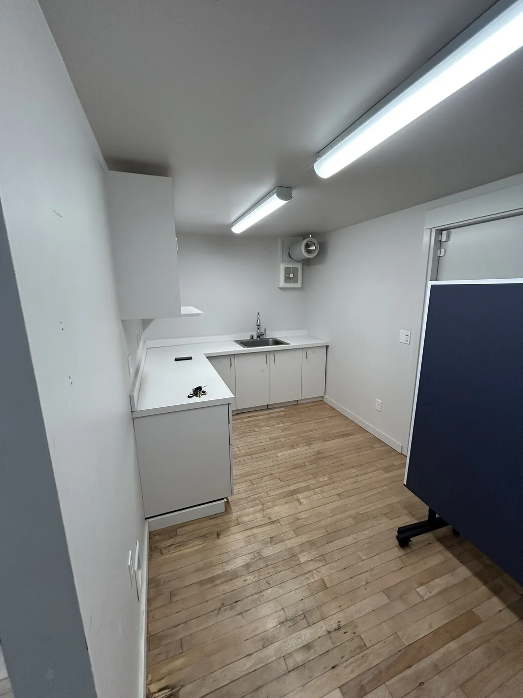 Finished commercial break-room build-out in Seattle, WA — new white cabinets, stainless sink, and wood-look flooring